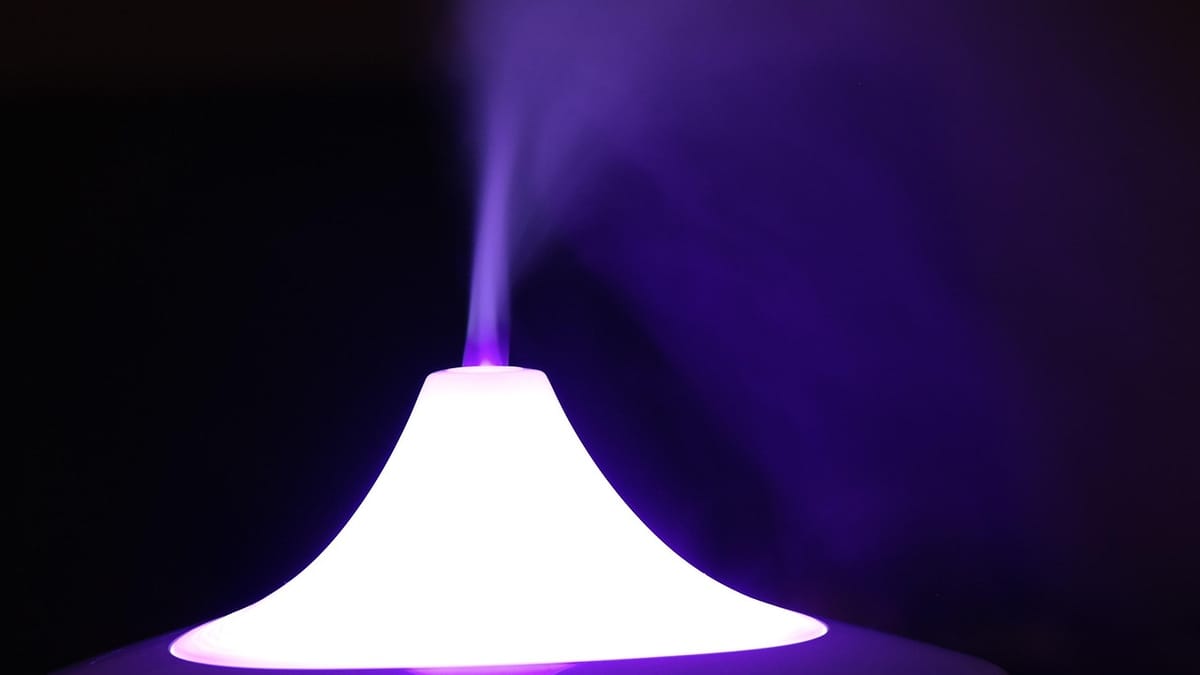 Diffuseur blanc éclairé de violet d'où s'élève un filet de brume, sur fond noir