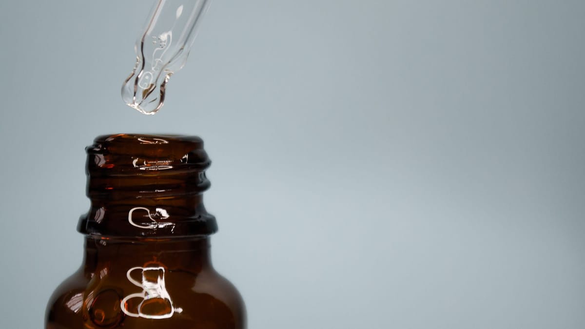 Compte-gouttes en verre au-dessus d'un flacon ambré d'huile essentielle