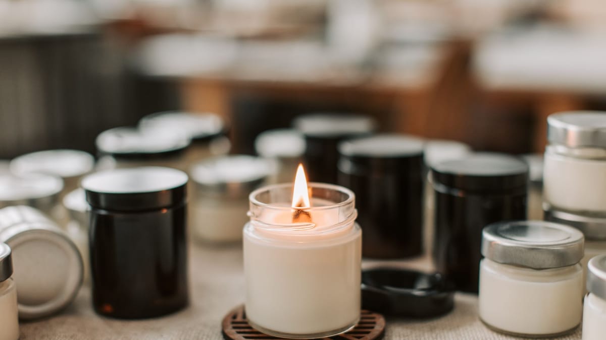 Bougie allumée dans un pot en verre, entourée de pots vides noirs et blancs