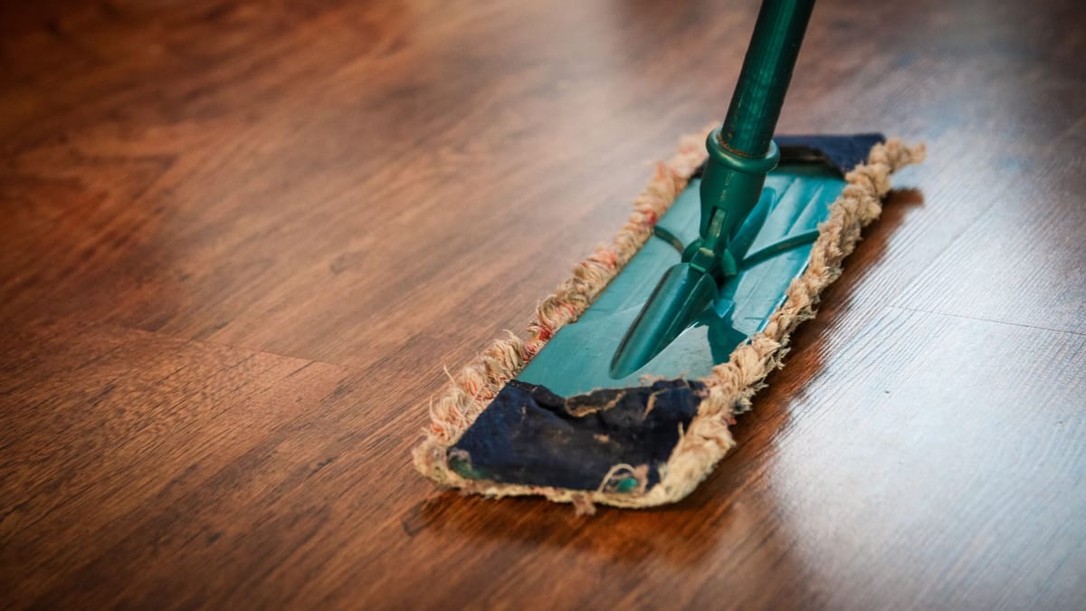 Balai plat à franges posé sur un parquet brun