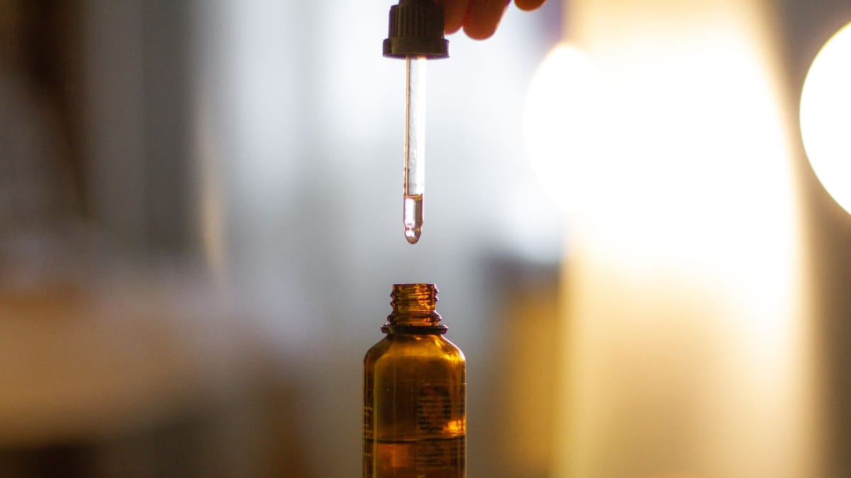 Pipette suspendue au-dessus d'un flacon en verre ambré, dans une lumière chaude